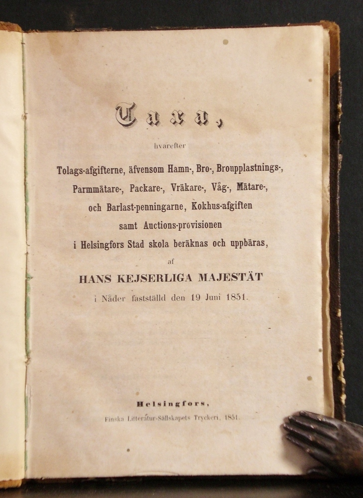 Taxa, hvarefter Tolags-afgifterne, äfvensom Hamn-, Bro-, Broupplastnings-, Parmmätare-, Packare-, Vräkare-, Våg-, Mätare-, och Barlast-penningarne, Kokhus-afgiften samt Auctions-provisionen i Helsingfors Stad skola beräknas och uppbäras, af Hans Kejserliga Majestät i nåder fastställd den 19 juni 1851